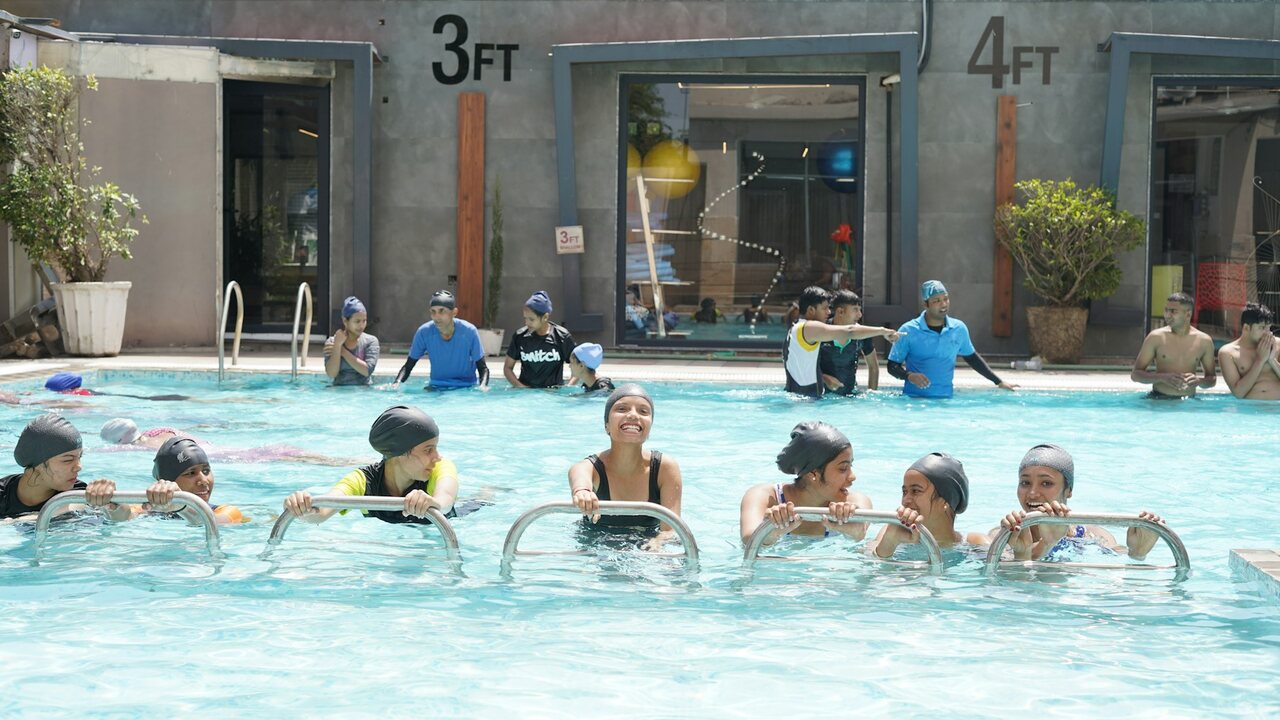 Swimmers holding the pool edge in a marked shallow lane during an instructor-led session